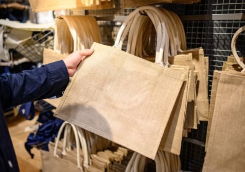 Male hand customer choosing brown jute handbag in craft shop. Reusable and Eco-friendly material bag for shopping. Buying concept
