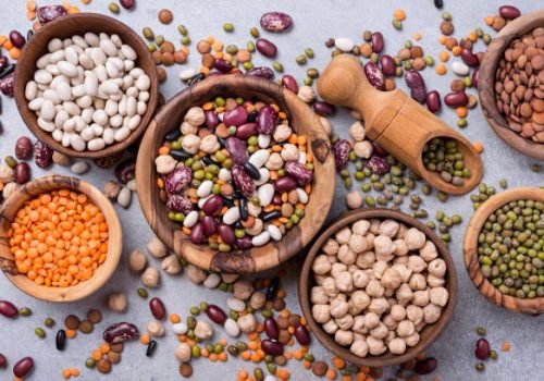 Top view of different beans, lentils, mung, chickpeas in wooden bowls for tasty meals on grey concrete background