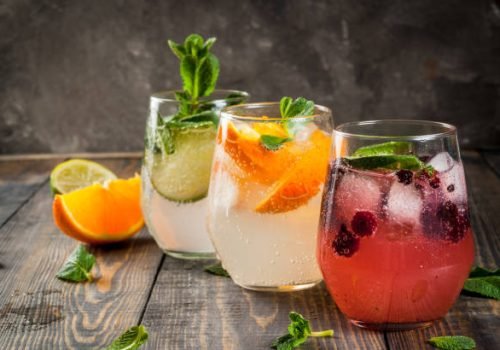 Selection of three kinds of gin tonic: with blackberries, with orange, with lime and mint leaves. In glasses on a rustic wooden background. Copy space